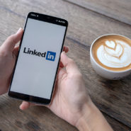 Hands holding a phone with LinkedIn screen and a latte