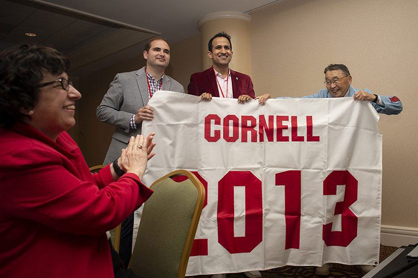 President Martha E. Pollack applauds as James Feld ’13 and Ankur Bajaj ’13 receive their Class of 2013 Reunion banner from Shigeo Kondo ’43.