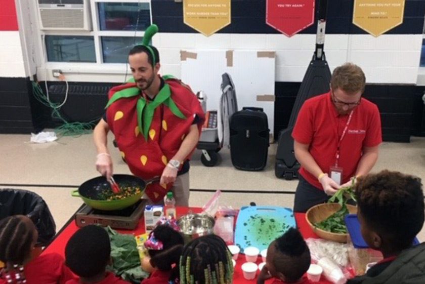 Dan Schiff ’05 (left) dressed as a strawberry, cooking up a nutritious stir fry at a Southeast D.C. elementary school in November 2019.