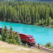 Red train on tracks next to bright blue lake