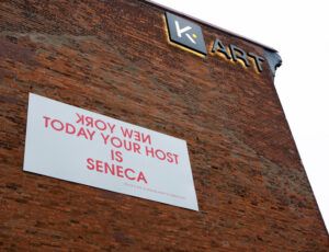 The side of the K Art gallery building features a “Native Host” sign by artist Edgar Heap of Birds.