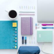 neatly organized and aesthetic office supplies, including a laptop, coffee cup, notebooks, paper clips, etc.
