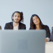 A group of four people wearing business clothing sit and speak to someone on a laptop in front of them.