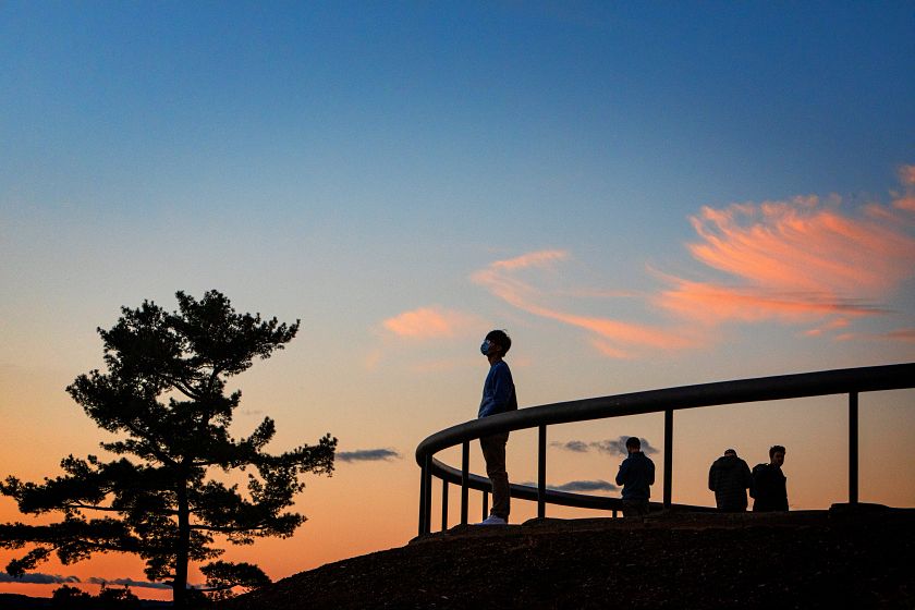 A silhouetted student stands at the top of Libe Slope, looking up. The sunset is orange and blue.
