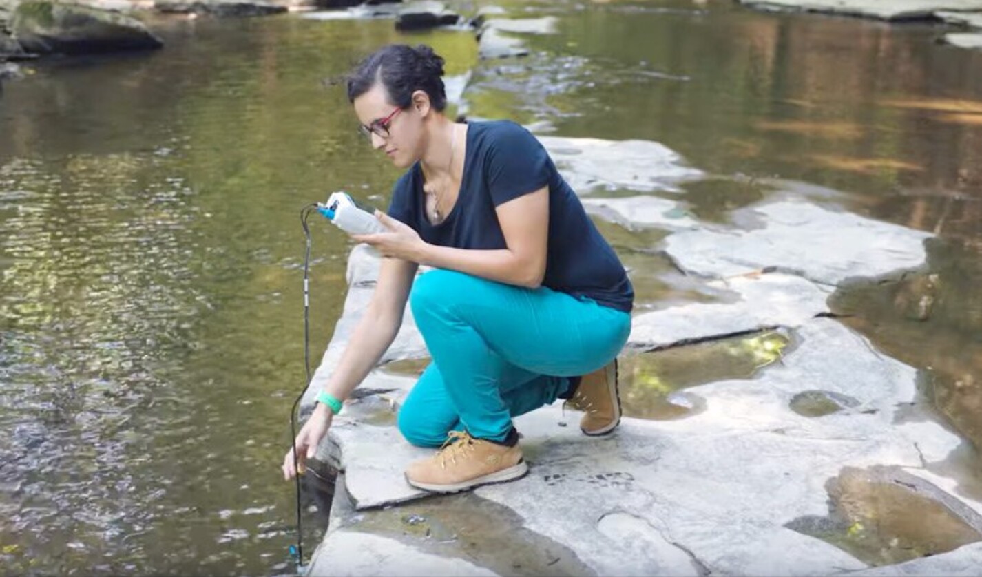 Nicole Fernandez, assistant professor of Earth and Atmospheric Sciences, takes a pH measurement in Cascadilla Creek near the Cornell Faculty Tennis Club.