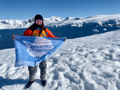 A person standing with a "7th Continent" flag in Antarctica.