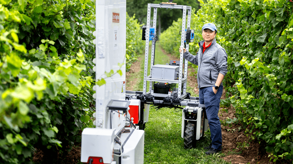 Yu Jiang poses with the PhytoPatholoBotas and UV light robot as part of the “Space for Ag Tour” at the Cornell Agritech campus.