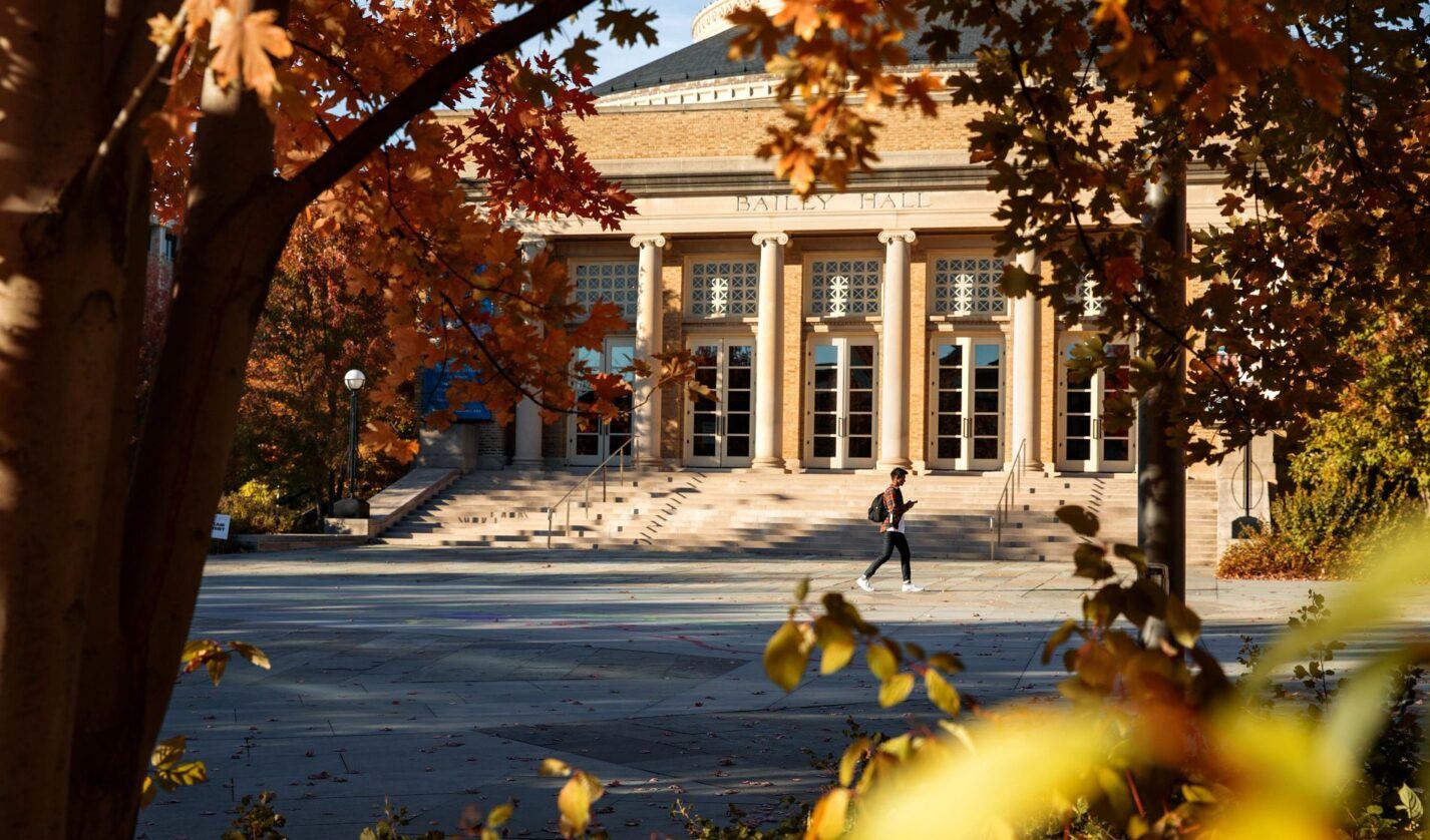 A student traverses Bailey Plaza amid fall foliage.