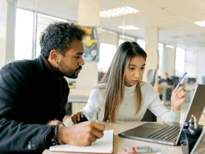 Two young professionals looking at a laptop and taking notes.