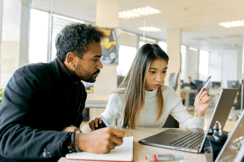 Two young professionals looking at a laptop and taking notes.