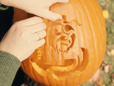 Hands carving out a Cornell stencil on a pumpkin
