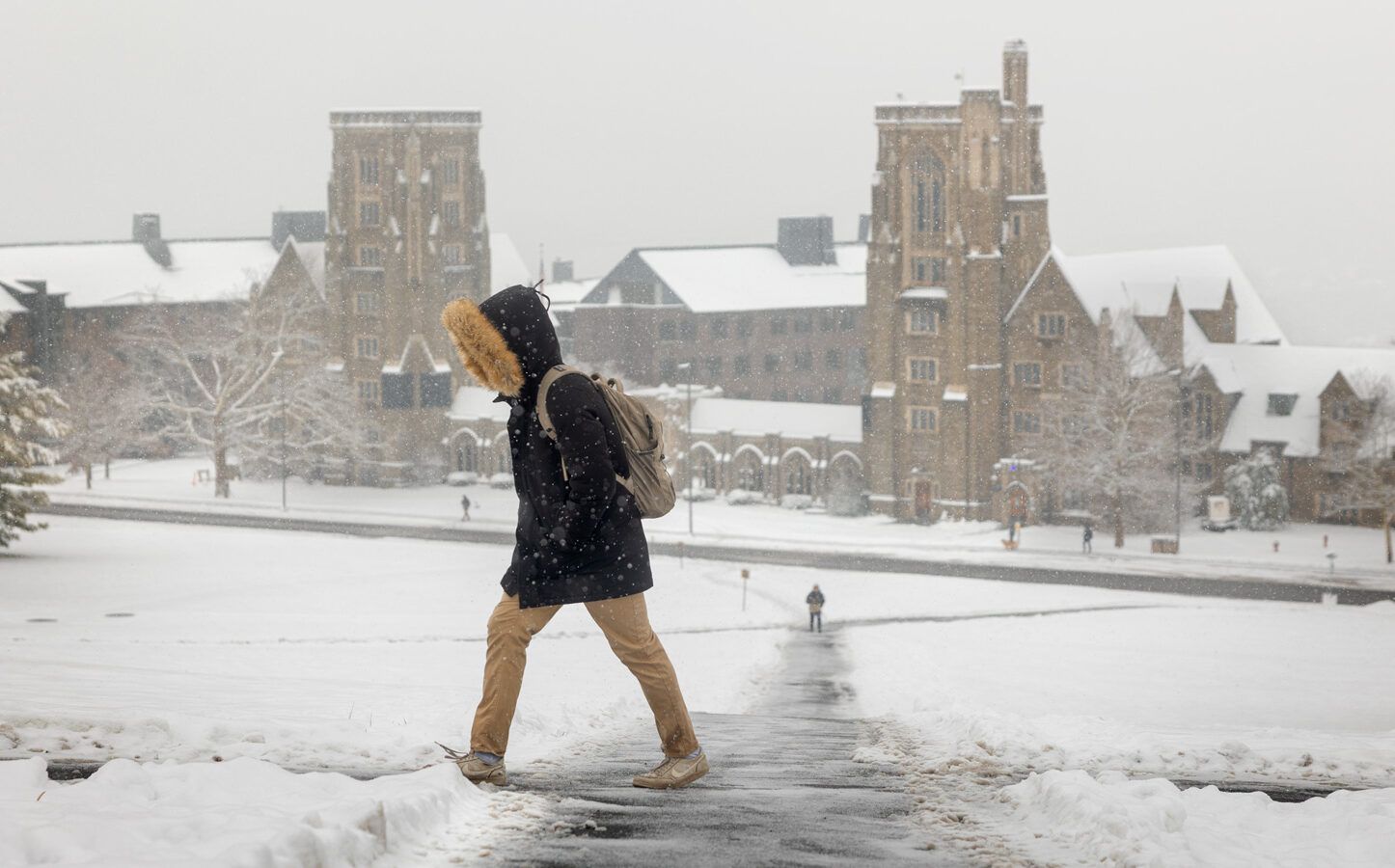 Students walk up libe slope in the winter with a person in a parka in the foreground