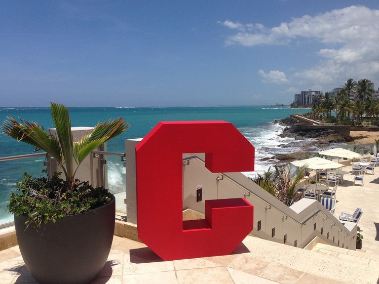 Large statue of the letter C on a patio, with view of beach